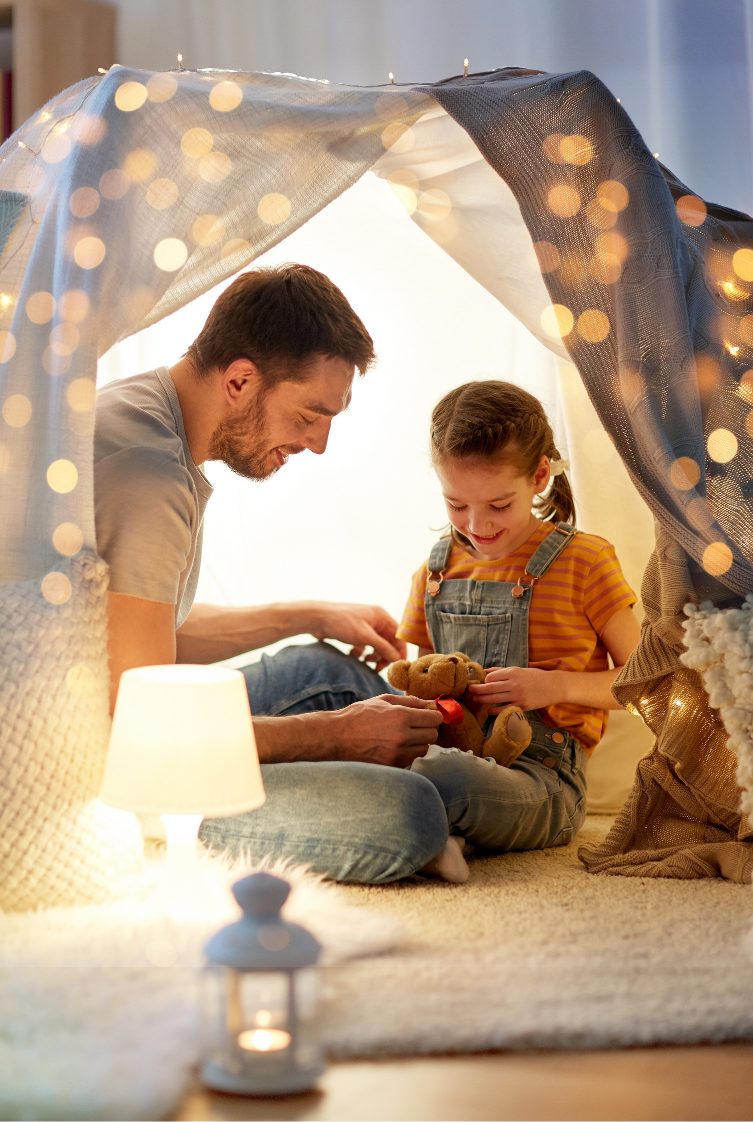 Father and daughter playing inside a homemade tent with string lights in the background